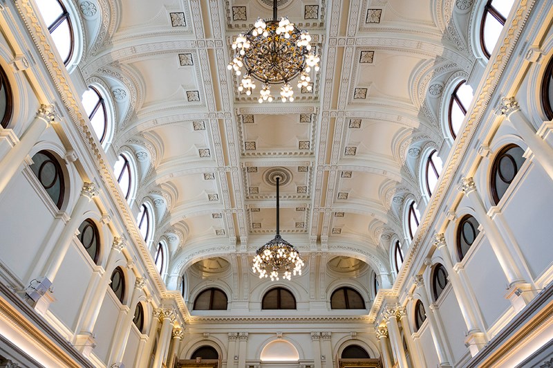 A large room with high ornate ceilings, arches and two chandeliers.